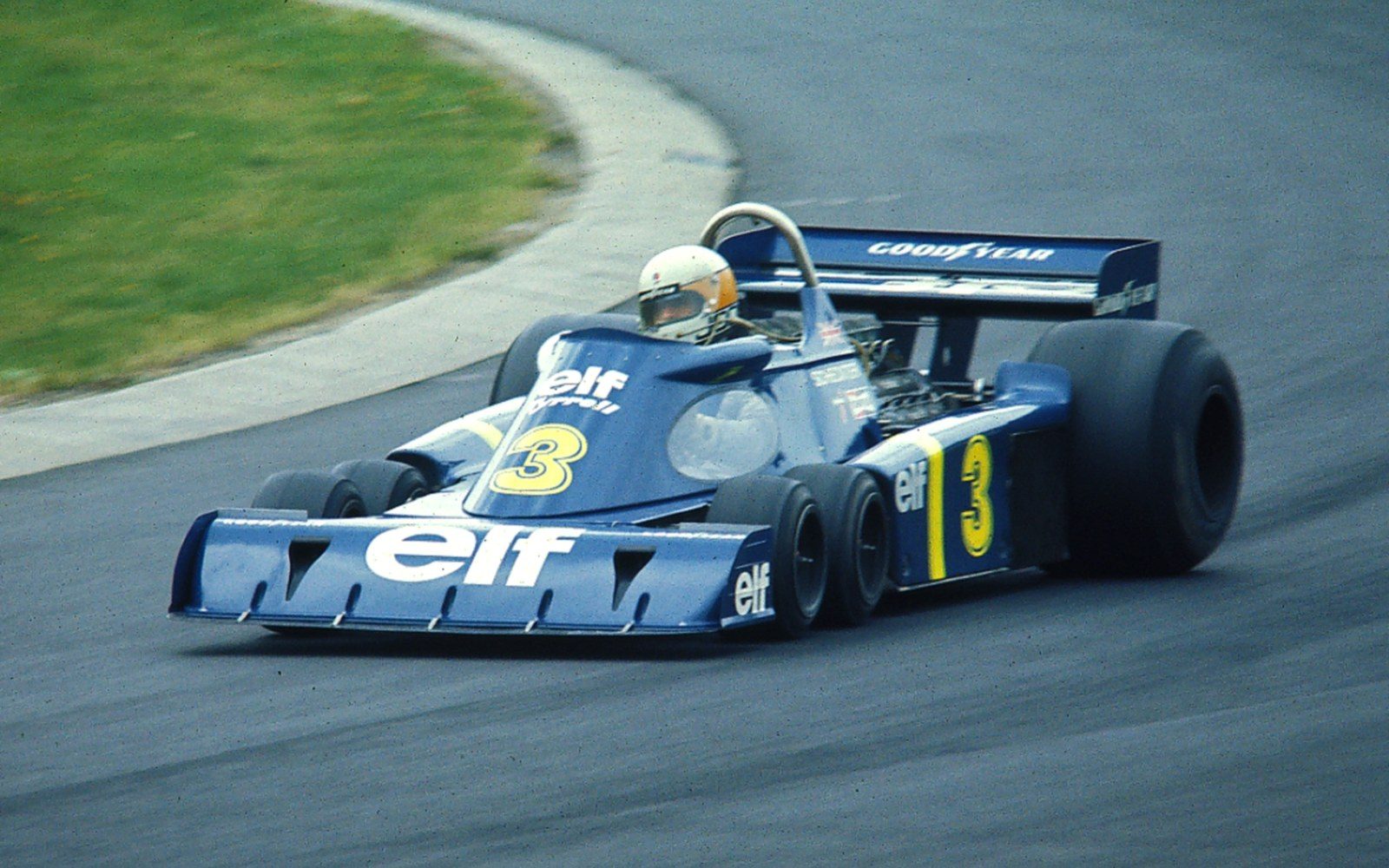 A six-wheeled Formula One car of the mid-1970s with four small front wheels, in a paddock