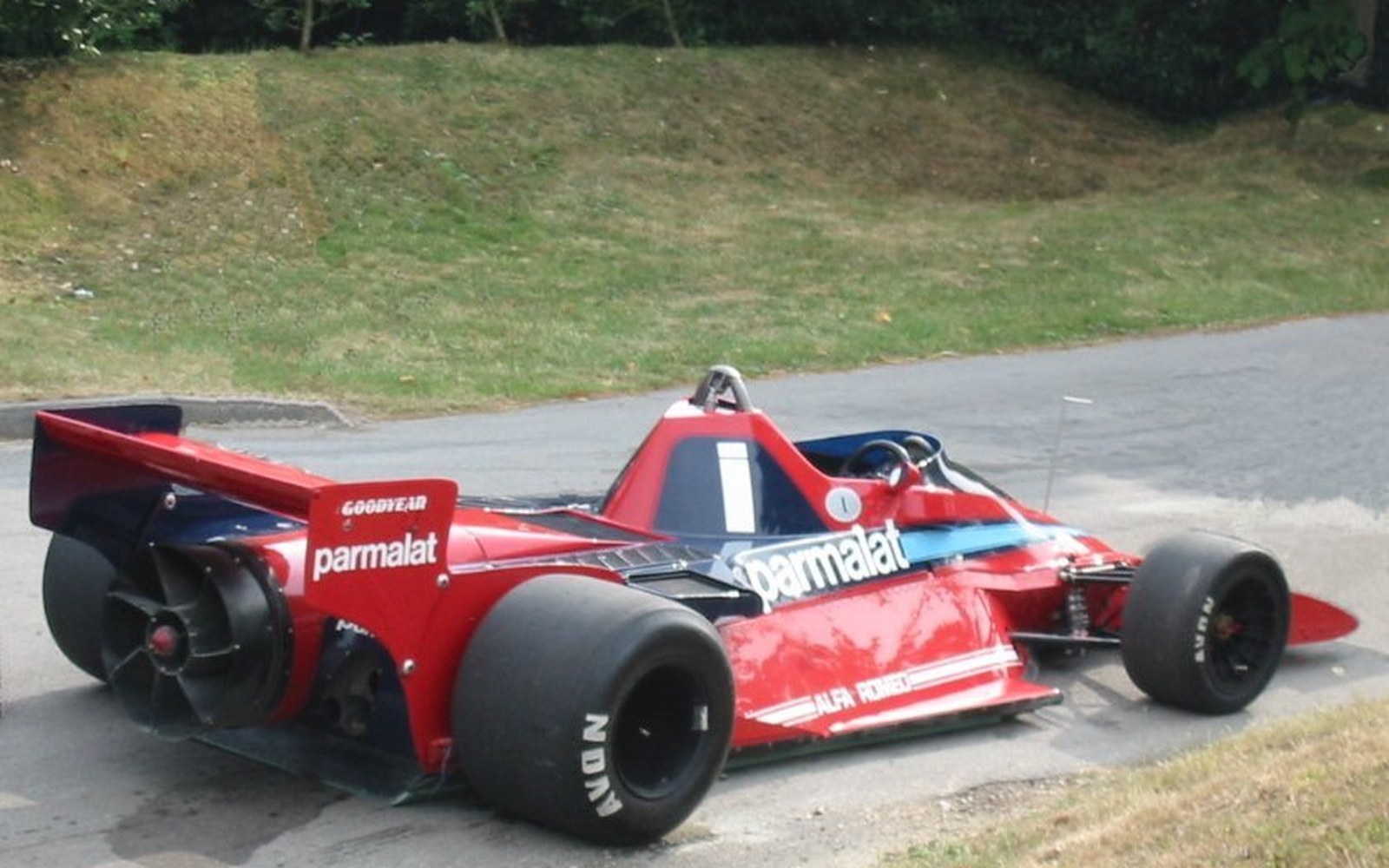 The rear of a 1970s Formula One car with a large horizontal fan mounted behind the engine, bodywork removed, pit garage light